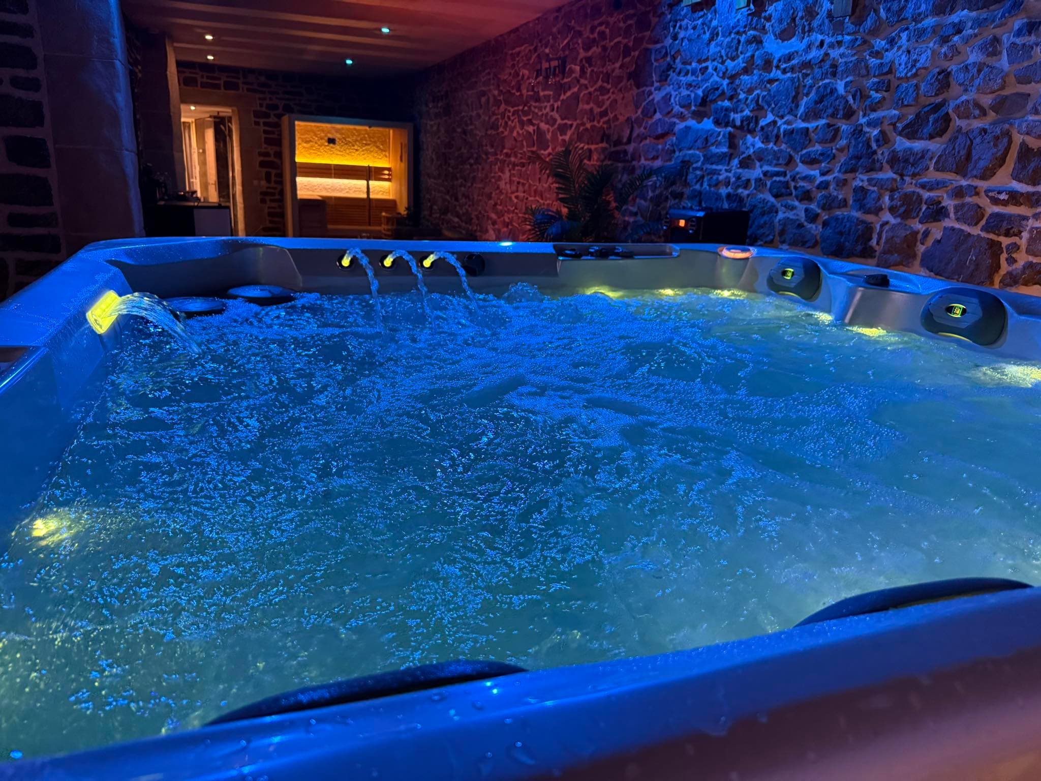 Jacuzzi privatif illuminé en bleu dans la salle en pierre d'Une bulle de sparadis