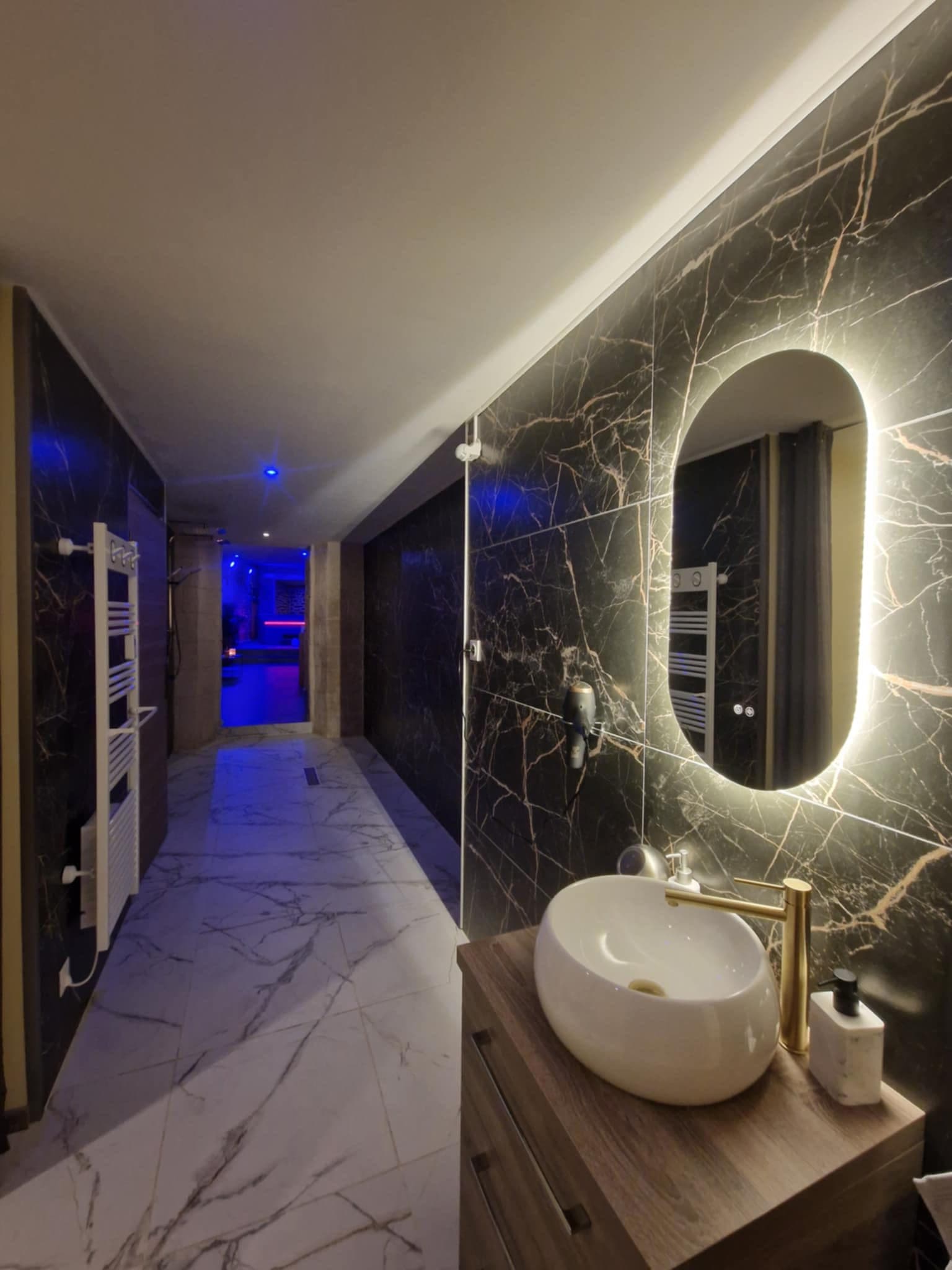 Salle de bain en marbre noir avec vasque ronde dorée et miroir rétroéclairé